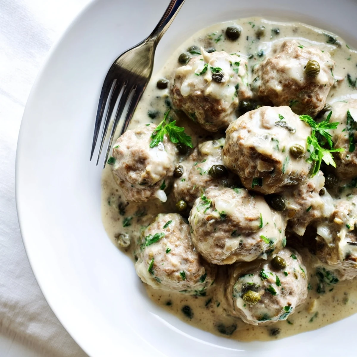 Zarte Kalb- und Schweinefleischbällchen in cremiger Kapernsauce serviert.